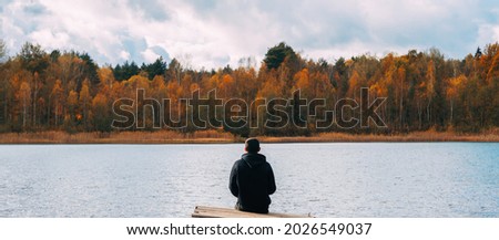 A lonely man on a bridge against the background of an autumn forest. The concept of depression, loneliness or autumn tourism