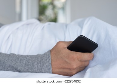 Lonely Man Or Patient In Bed Holding Mobile Smartphone Waiting For Call, Close Up