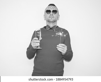 lonely man posing near wall with glass of champagne and lighting sparkler in hand. boy wearing butterfly and has 2021 written on forehead. celebrating silvester or new year 2021 at home quarantine.