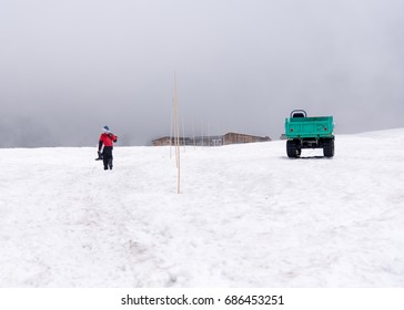 A Lonely Man In Red Jacket Walking Alone On A Frozen Clumsy Snowing Day Along With A Bright Green Truck That Driving In The Middle Of The Snow