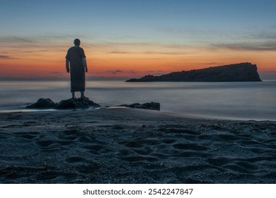 Lonely man relaxing on the beautiful beach at sunset. Sun reflected on beach, Lonely man stands on beach looks towards sun light. African Arab man meets sunset on beach, silhouette of person walking. - Powered by Shutterstock