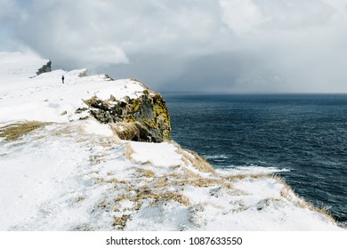 Lonely Man Sillhouette On A High Snow-covered Cliff Near The Ocean. Latrabjarg, Iceland