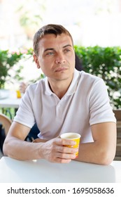 A Lonely Man Sits In A Summer Cafe. A 35-40 Year Old Man Is A Lonely Sad Man Sitting With A Glass Of Coffee In A Street Cafe.