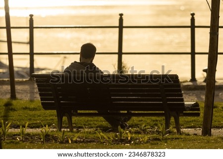 Lonely man sitting on a bench at early sunset