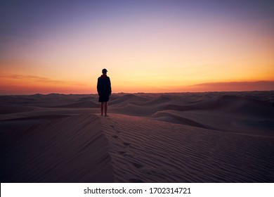 Lonely man standing on sand dune in the middle of desert at dusk. Abu Dhabi, United Arab Emirates