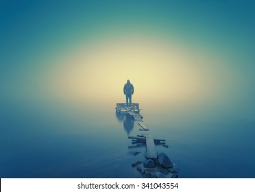 Lonely man, standing on the wooden jetty in the autumn foggy river with stones gangway.  - Powered by Shutterstock