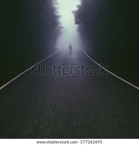 Lonely man walking down the foggy forest road
