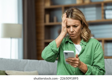 Lonely mature woman alone close up holding phone upset and depressed reading bad news on smartphone online in living room close up. - Powered by Shutterstock