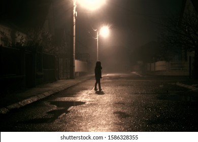 Lonely Mystery Girl On Empty Street. City Street At Night In Dense Fog. Thick Smog On A Dark Street. Scary Scene Silhouette Of Running Child Like A Ghost Through Misty Rainy Night