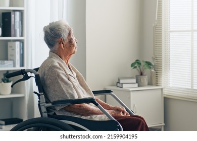 Lonely old senior Asian woman, sitting alone in the room, looking through the window