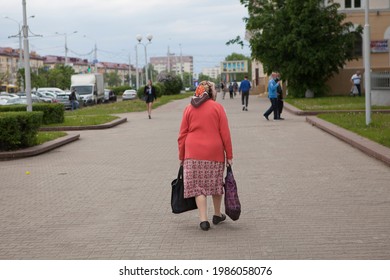 Lonely Old Woman Retired Walking Down The Street With Bags. Back View. 05.28.2021. Minsk, Belarus.