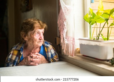 Lonely old woman sitting by the window in his cottage.