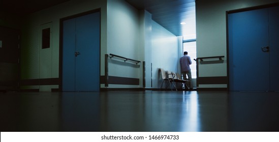 Lonely Patient In Full Length In Modern Hospital Waiting Lobby Room Near The Window As He Waits For Good Or Bad News From His Doctor - Blue Hospital Atmosphere