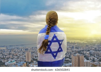 Lonely patriot jewish girl standing and looking at the sunrise in Haifa with the flag of Israel wrapped around her. Newcomer life and immigration to Israel concept.
