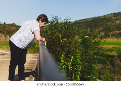 Lonely Person Looking Over A Bridge's Edge - Old Woman Laying On Bridge Balustrade Looking Down At River