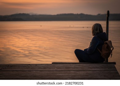 A Lonely Person Sitting On A Pier And Looking At The Beautiful 
Pink Sunset