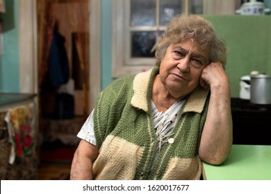 Lonely Poor Elderly Woman At Home In The Kitchen