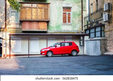 lonely red car is waiting for his master driver in the empty courtyard green multi-storey old house in a sunny day, empty car parked on a makeshift yard parking