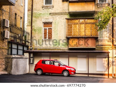 lonely red car is waiting for his master driver in the empty courtyard green multi-storey old house in a sunny day, empty car parked on a makeshift yard parking