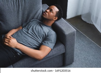 Lonely Sad African American Man Lying On Sofa At Home
