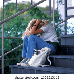 Lonely and sad teenage girl stting outside on a stone staircase hiding behind her arms - Powered by Shutterstock