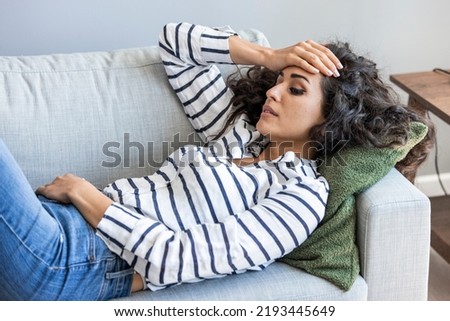 Lonely sad woman deep in thoughts sitting daydreaming or waiting for someone in the living room with a serious expression, she is pensive and suffering from insomnia sitting on couch