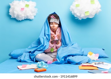 Lonely Sad Woman Poses Under Blanket Drinks Hot Beverage Dressed In Soft Pajama Does Homework At Home Sits Crossed Legs On Bed Lears Assignment Makes Notes Isolated Over Blue Wall With Clouds Above