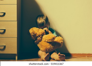 Lonely scared boy sitting in corner, hugging his teddy bear and crying. Child abuse