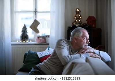 Lonely Senior Man Sitting On Sofa Indoors At Christmas, Solitude Concept.