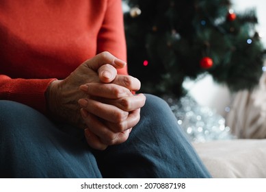 Lonely senior woman sitting at home in Christmas celebration. Close-up of an elderly woman's hand against background of decorated Christmas tree. Loneliness, sad holiday concept.