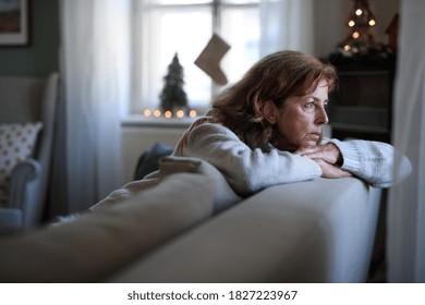 Lonely senior woman sitting on sofa indoors at Christmas, solitude concept.
