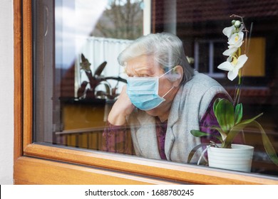 lonely senior woman with surgical mask sitting on a window plane at home, coronavirus and covid-19 provisions