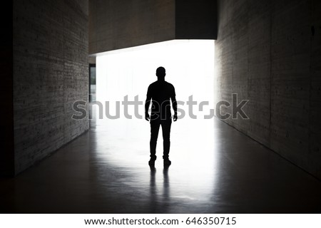 Lonely silhouette in dark architecture with light background. Full-length portrait of man on his back.