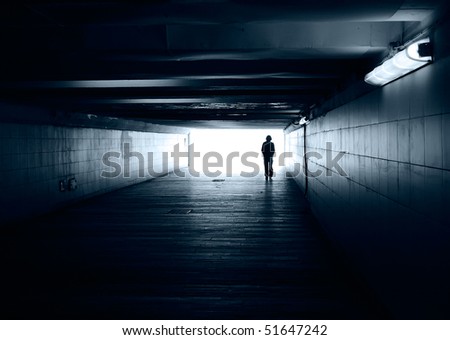 Lonely silhouette in dark subway tunnel goes towards the light