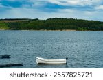 Lonely, single boat drifting along a lake, reservoir. Hills in the countryside. Peaceful waters. Background woodland, forest. Great Britain. UK.