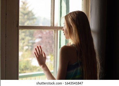 Lonely teenage girl waiting near the hazy window inside the room
