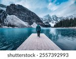 Lonely traveler man walking on pier surrounded by Rocky mountains on Moraine Lake at Banff national park, Alberta, Canada