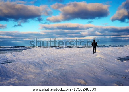 Lonely traveler on the snow-covered coast of the frozen sea in the evening