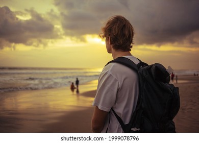 A lonely traveler with a rucksack watching golden sunset with stormy clouds on a tropical beach in Asia.