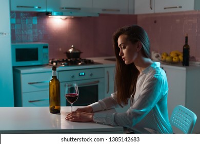 Lonely, Unhappy, Sad Beautiful Young Woman In A Blouse With Glass Of Red Wine Is Drinking Alone In Evening At Home. Female Alcoholism And Alcohol Addiction