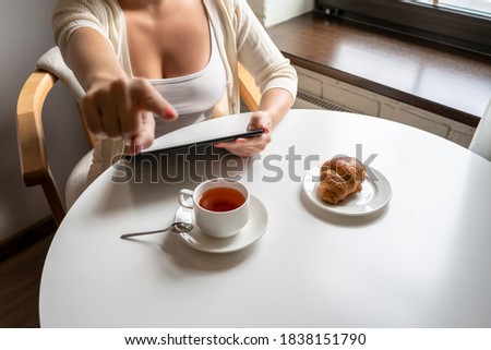 Lonely woman freelancer enjoying having breakfast with cup of coffee working on tablet sitting near window in cafe at morning. View on bust of female