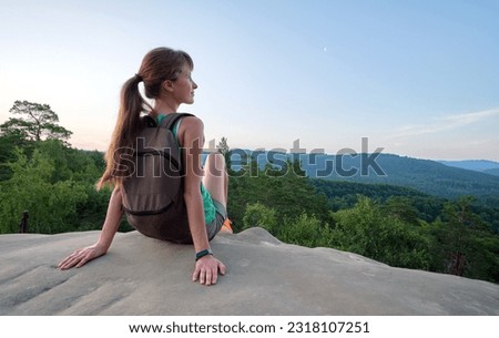 Lonely woman hiker sitting alone on rocky mountain top enjoying view of morning nature on wilderness trail. Active lifestyle concept