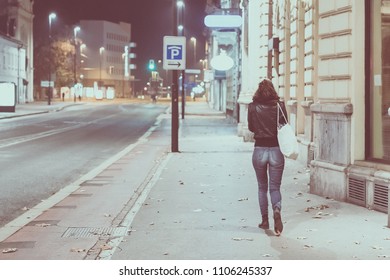 Lonely Woman In Jeans And Jacket Is Walking Away From The Camera On An Empty City Street At Night