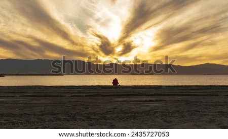 lonely woman resting on the beach, watching the sunset on the beach, overlooking the bay and the nearby town