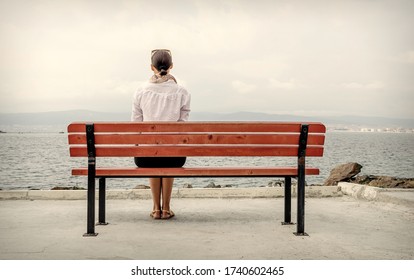 A Lonely Woman Sits On A Bench By The Water. Toned Image.