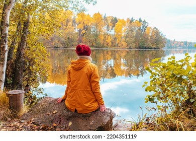 Lonely woman is sitting on the shore of a forest lake. Autumn landscape, calmness, tranquility, travel.  - Powered by Shutterstock