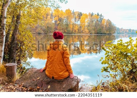 Lonely woman is sitting on the shore of a forest lake. Autumn landscape, calmness, tranquility, travel. 