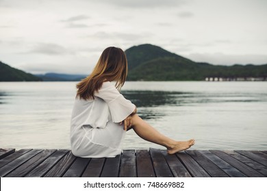 Lonely woman sitting on wooden pier and looking at the lake - Powered by Shutterstock