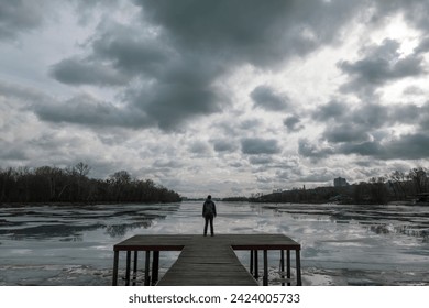 Lonely woman standinng on the wooden pier looking at cloud reflections in the cold water. Dramatic photo about hard time, difficult life choices and depressive mood - Powered by Shutterstock