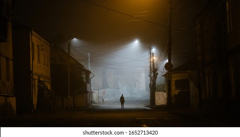 Lonely woman walking in a foggy old city in city street lights